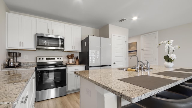kitchen featuring white cabinets, appliances with stainless steel finishes, a sink, a breakfast bar area, and light wood-type flooring