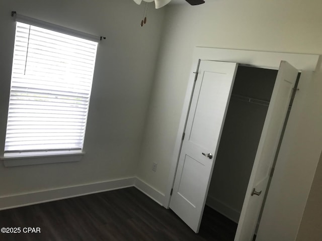 unfurnished bedroom featuring a closet, multiple windows, baseboards, and dark wood finished floors