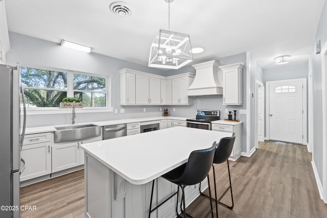 kitchen featuring visible vents, appliances with stainless steel finishes, a sink, custom range hood, and a notable chandelier