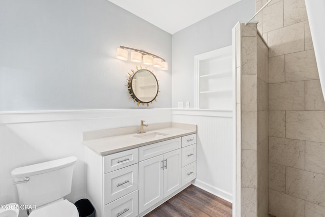 full bath with a tile shower, vanity, a wainscoted wall, toilet, and wood finished floors