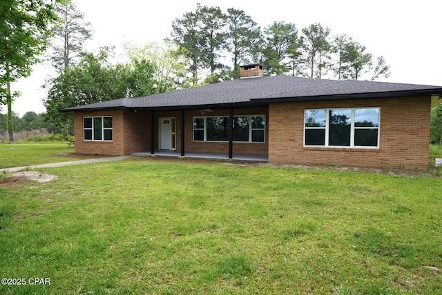 back of house featuring a yard, a chimney, brick siding, and a patio area