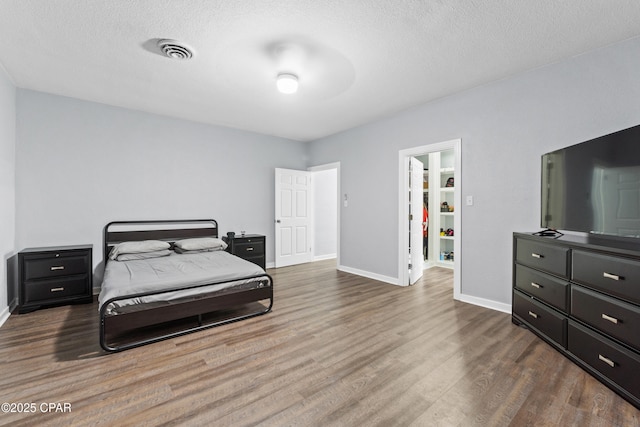 bedroom with visible vents, baseboards, a textured ceiling, and wood finished floors
