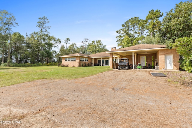 ranch-style home with a chimney, dirt driveway, a front lawn, an attached carport, and brick siding