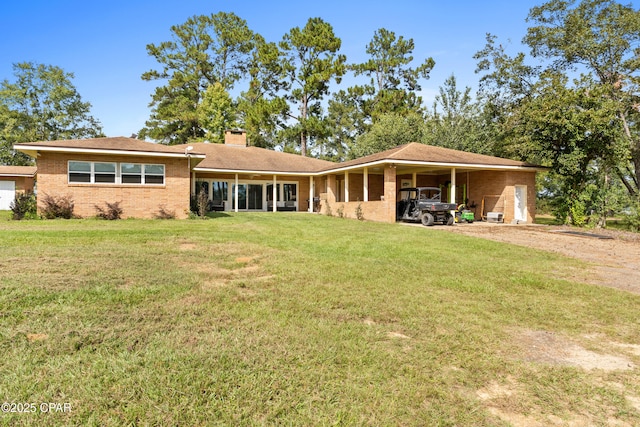rear view of property with dirt driveway, a lawn, brick siding, a chimney, and an attached carport