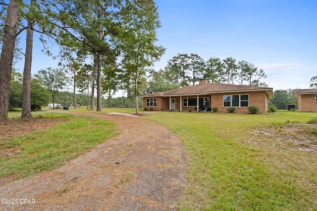 ranch-style house featuring a chimney, driveway, a front yard, and brick siding