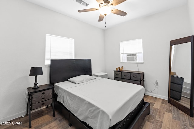 bedroom with visible vents, baseboards, a ceiling fan, cooling unit, and wood finished floors
