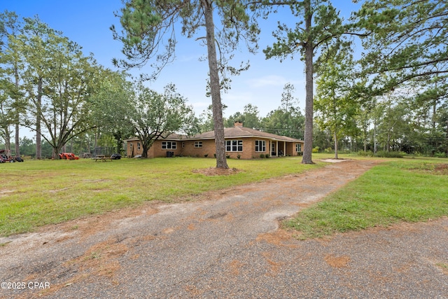 ranch-style home featuring a front yard, brick siding, driveway, and a chimney