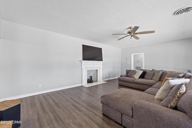 living area with baseboards, a fireplace, a ceiling fan, dark wood-type flooring, and visible vents