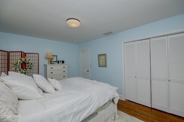 bedroom featuring wood finished floors, visible vents, and a closet