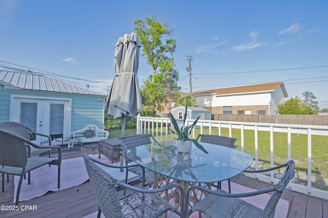 wooden terrace with outdoor dining space, french doors, fence, an outbuilding, and a yard