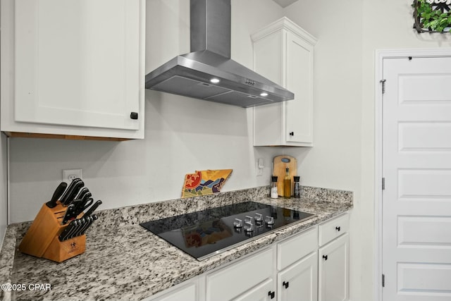 kitchen featuring black electric cooktop, light stone counters, white cabinetry, and wall chimney exhaust hood