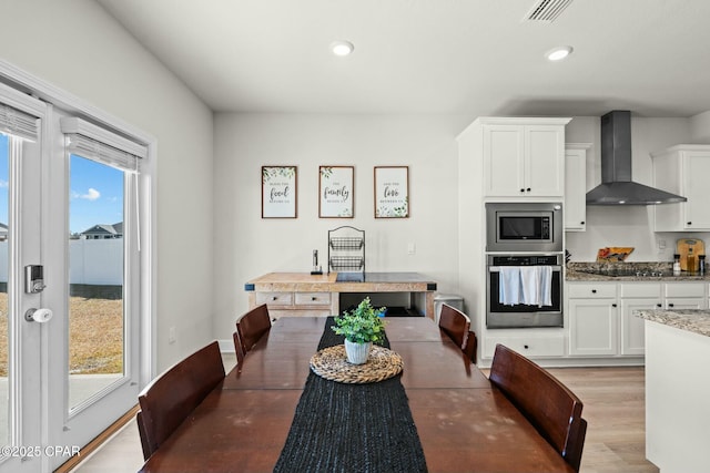 kitchen with visible vents, wall chimney exhaust hood, light stone counters, stainless steel appliances, and white cabinetry