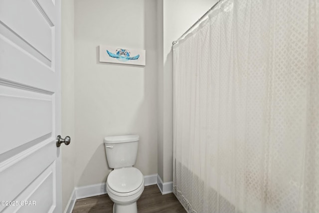 bathroom with baseboards, curtained shower, toilet, and wood finished floors