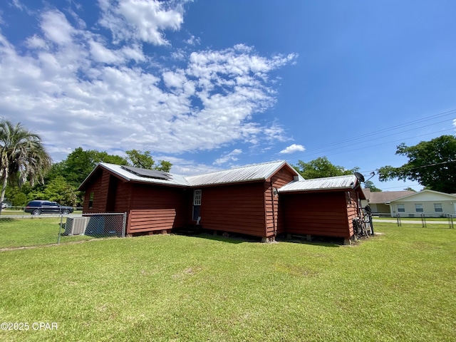 view of side of home with metal roof, solar panels, fence, and a lawn