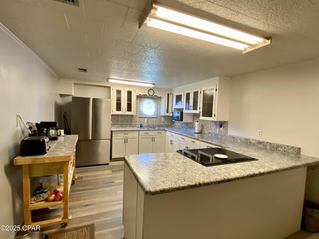 kitchen with black electric stovetop, a peninsula, white cabinetry, freestanding refrigerator, and a sink