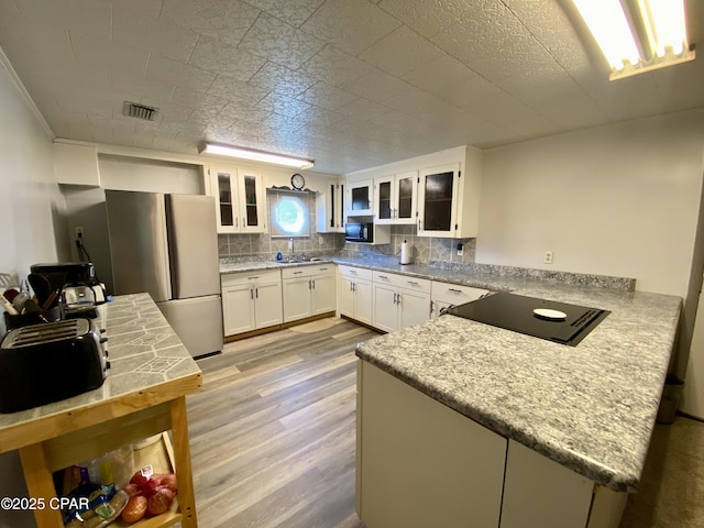 kitchen with white cabinets, stovetop, freestanding refrigerator, a peninsula, and light wood-style flooring
