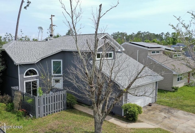 exterior space featuring fence, a shingled roof, concrete driveway, a lawn, and a garage