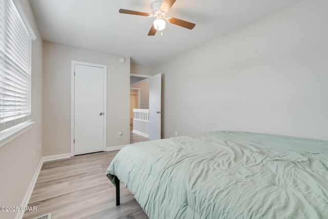 bedroom featuring ceiling fan, baseboards, multiple windows, and light wood-style floors