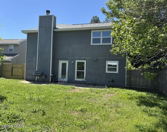 back of house with a lawn, a fenced backyard, and a chimney
