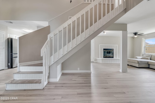 stairway with a ceiling fan, wood finished floors, a towering ceiling, baseboards, and visible vents