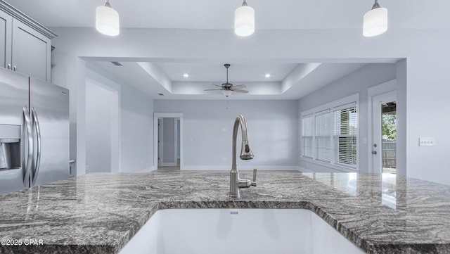 kitchen featuring a sink, dark stone countertops, a raised ceiling, a ceiling fan, and stainless steel refrigerator with ice dispenser