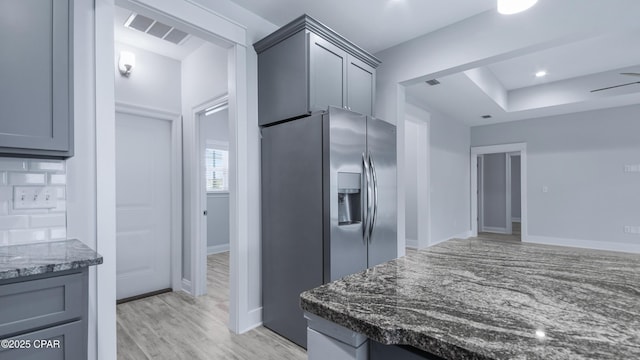 kitchen featuring stainless steel refrigerator with ice dispenser, visible vents, light wood-type flooring, and dark stone counters