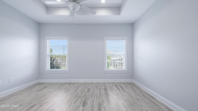 spare room with a ceiling fan, a raised ceiling, wood finished floors, and baseboards