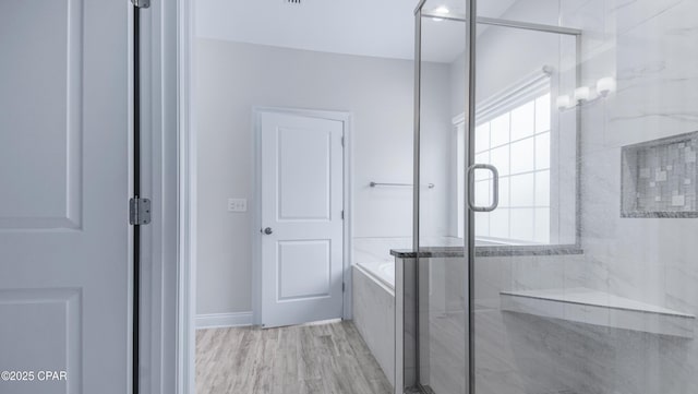 bathroom featuring a bath, a marble finish shower, and wood finished floors