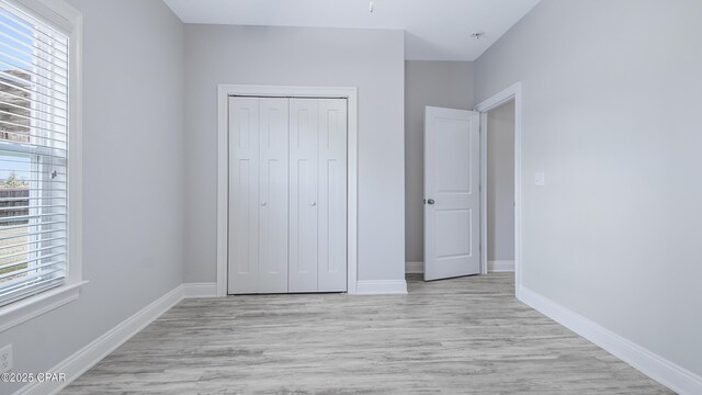 unfurnished bedroom featuring a closet, baseboards, and light wood-style floors