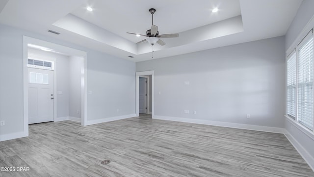 spare room with ceiling fan, a raised ceiling, light wood-type flooring, visible vents, and baseboards