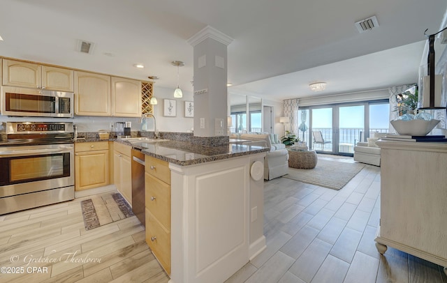 kitchen featuring light brown cabinetry, stainless steel appliances, visible vents, a sink, and open floor plan