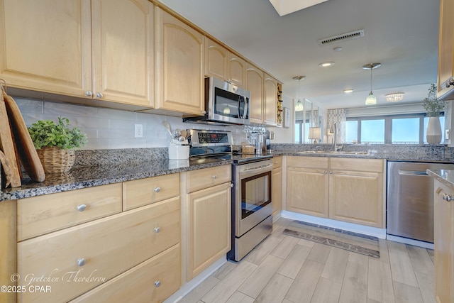 kitchen with stainless steel appliances, visible vents, light brown cabinets, a sink, and dark stone counters