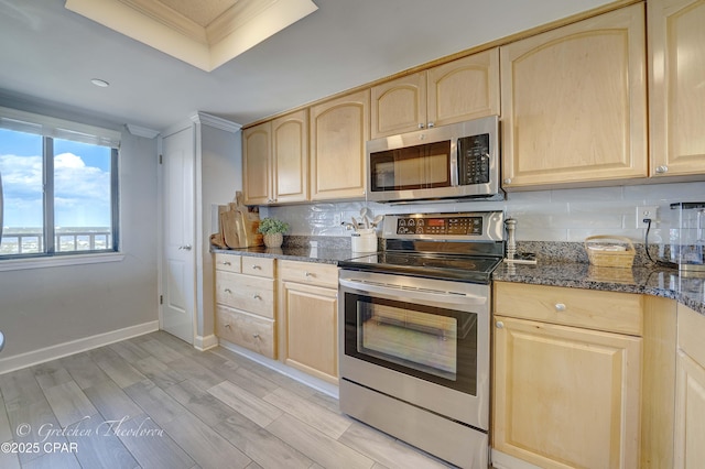 kitchen featuring dark stone counters, appliances with stainless steel finishes, light brown cabinets, and light wood finished floors