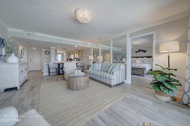 living room with light wood-style floors, visible vents, crown molding, and baseboards