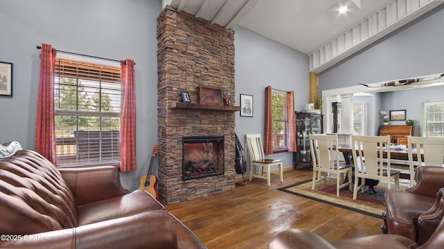 living room featuring wood-type flooring, a stone fireplace, and high vaulted ceiling