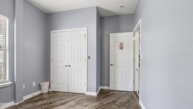 unfurnished bedroom featuring baseboards, multiple windows, wood finished floors, and a closet