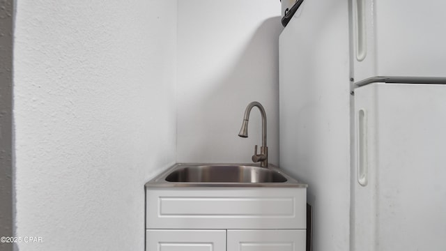 details featuring a sink, a textured wall, and freestanding refrigerator