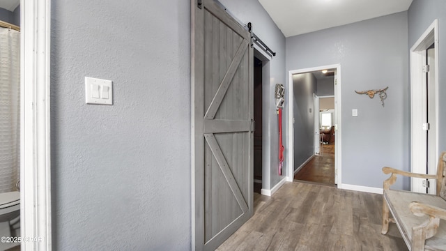 hall featuring baseboards, a textured wall, a barn door, and wood finished floors