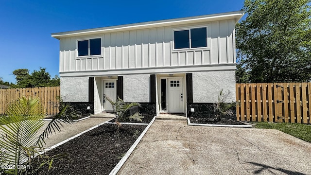view of front facade with stucco siding, fence, and board and batten siding
