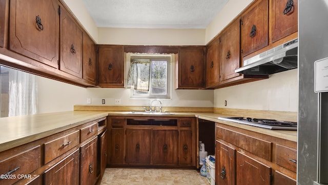 kitchen featuring stainless steel gas stovetop, under cabinet range hood, light countertops, a sink, and a textured ceiling