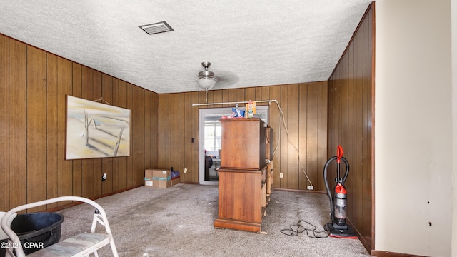 unfurnished office featuring carpet, wood walls, visible vents, baseboards, and a textured ceiling