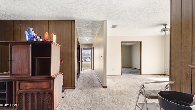 corridor featuring light carpet, a textured ceiling, visible vents, and baseboards