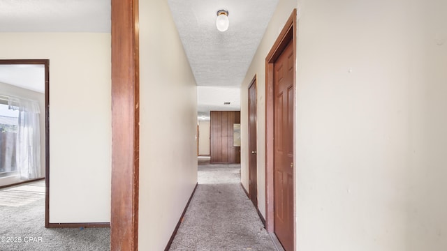 corridor featuring baseboards, carpet floors, and a textured ceiling