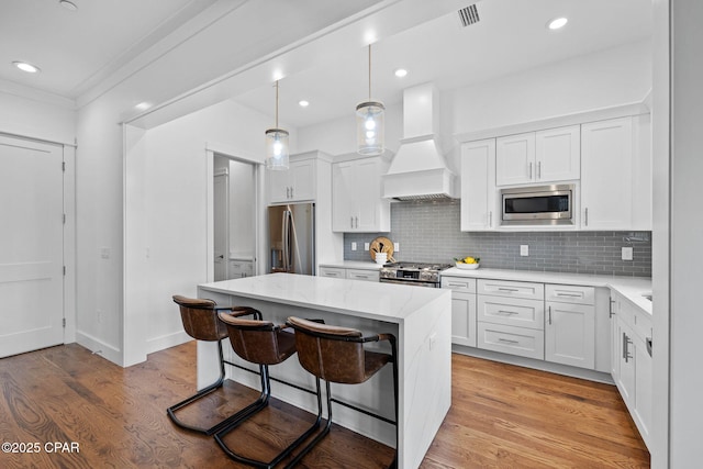 1502 Match Point Ln Unit 402, Panama City Beach, FL 32413 - kitchen with stainless steel appliances, wall chimney exhaust hood, a kitchen island, a kitchen breakfast bar, and white cabinetry