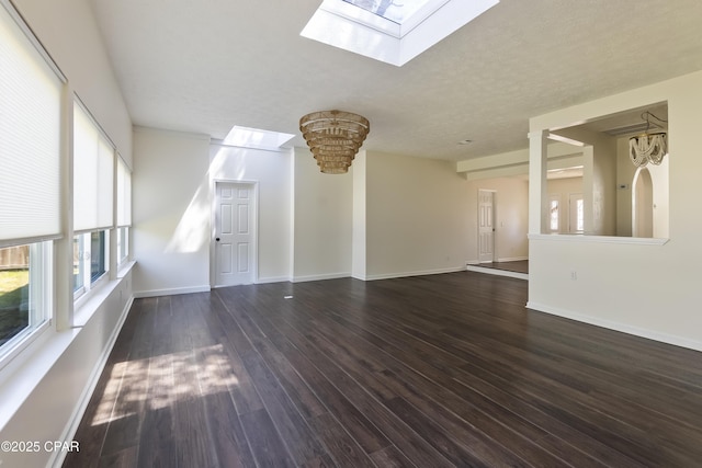unfurnished living room with a skylight, baseboards, and dark wood-style flooring
