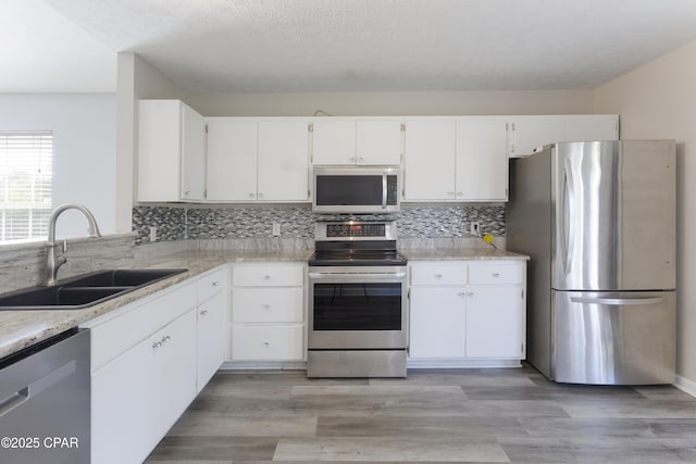 kitchen featuring tasteful backsplash, a sink, stainless steel appliances, white cabinetry, and light wood-type flooring