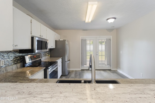 kitchen with baseboards, light wood-type flooring, tasteful backsplash, a sink, and stainless steel appliances