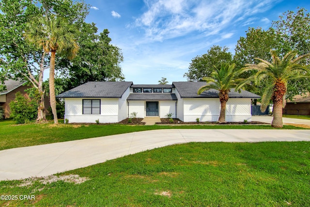 view of front facade featuring roof with shingles, a front yard, and curved driveway