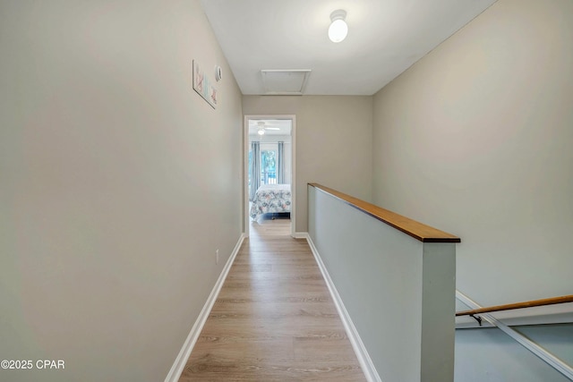 corridor with baseboards, attic access, light wood-type flooring, and an upstairs landing