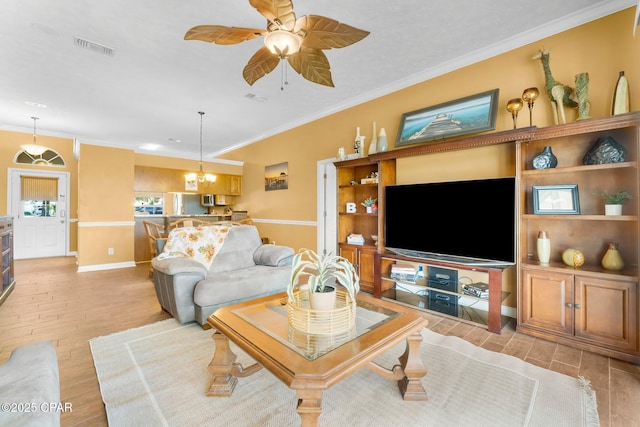living area featuring baseboards, ornamental molding, visible vents, light wood finished floors, and ceiling fan with notable chandelier